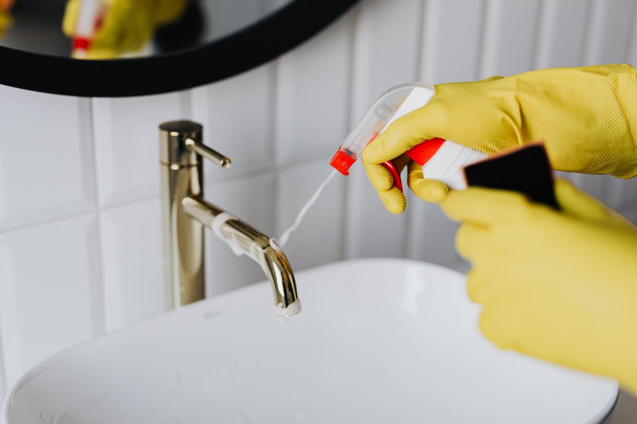 who-we-are From above anonymous housekeeper in yellow rubber gloves spraying cleaner to chrome water faucet in bathroom